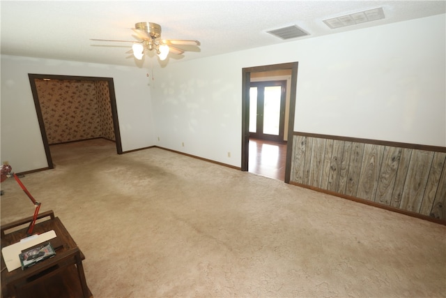 carpeted empty room featuring ceiling fan and wood walls