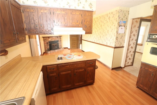 kitchen featuring kitchen peninsula, a wood stove, white appliances, and light wood-type flooring