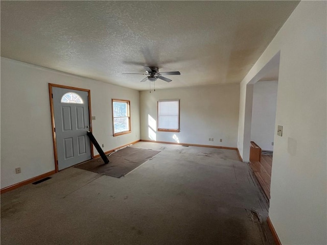 foyer entrance with ceiling fan, light carpet, and a textured ceiling