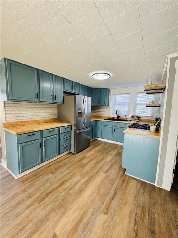 kitchen with wood counters, sink, backsplash, stainless steel fridge, and light hardwood / wood-style flooring