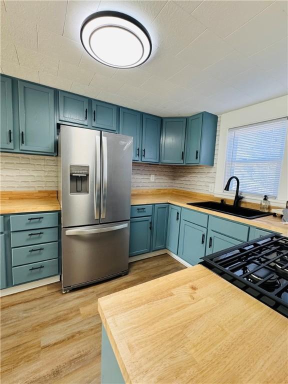 kitchen featuring wood counters, sink, backsplash, stainless steel refrigerator with ice dispenser, and light hardwood / wood-style flooring