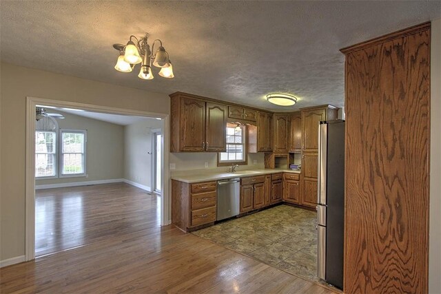 kitchen with a textured ceiling, light countertops, light wood-style flooring, appliances with stainless steel finishes, and a sink