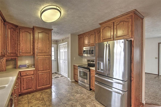 kitchen featuring a textured ceiling, baseboards, stainless steel appliances, a sink, and brown cabinetry