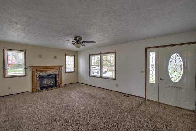 unfurnished living room with a wealth of natural light, visible vents, carpet flooring, and a ceiling fan