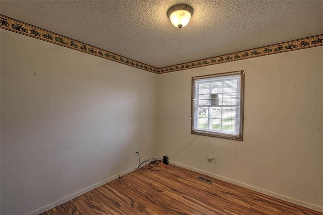 empty room with baseboards, visible vents, a textured ceiling, and wood finished floors