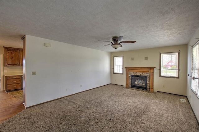 unfurnished living room with a fireplace, a textured ceiling, ceiling fan, and light colored carpet