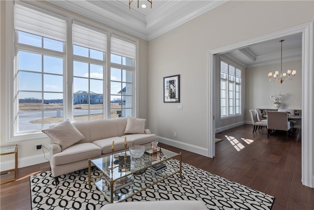 living room featuring dark wood-style flooring, baseboards, ornamental molding, a raised ceiling, and an inviting chandelier