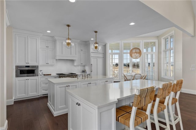 kitchen featuring a center island with sink, white cabinets, appliances with stainless steel finishes, decorative light fixtures, and light countertops