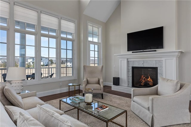 living room featuring high vaulted ceiling, a fireplace, baseboards, and wood finished floors