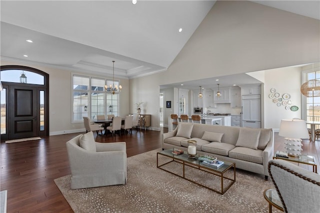 living area with a chandelier, high vaulted ceiling, baseboards, dark wood finished floors, and crown molding