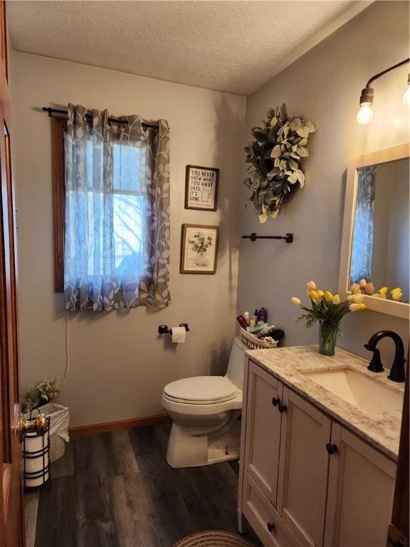 bathroom featuring baseboards, toilet, vanity, wood finished floors, and a textured ceiling