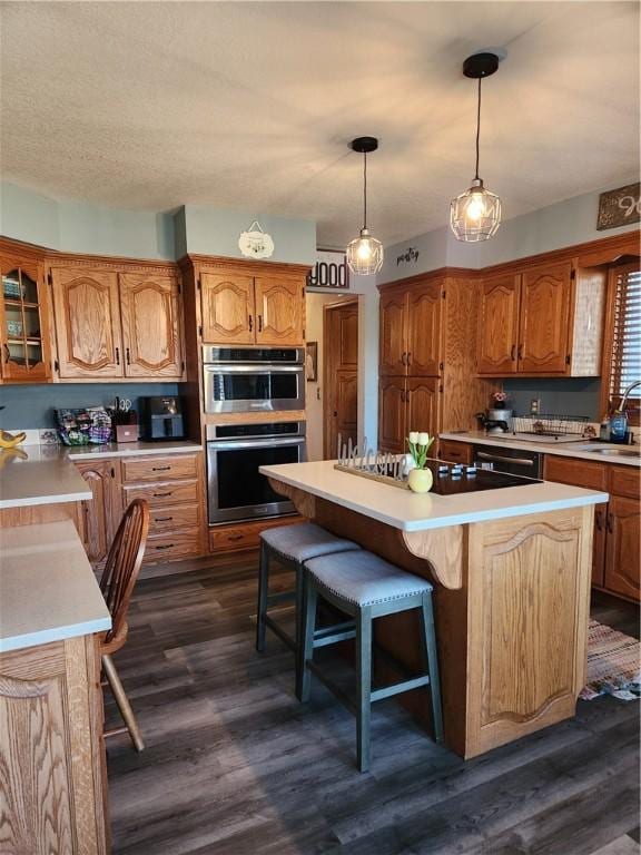 kitchen with a kitchen breakfast bar, a kitchen island, double oven, light countertops, and dark wood-style flooring