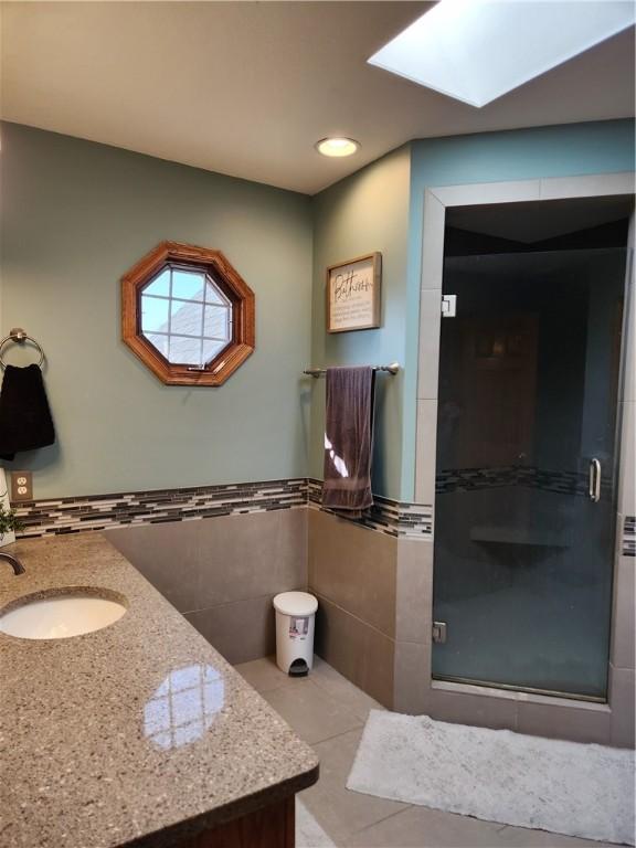 full bath featuring vanity, a skylight, a stall shower, tile patterned flooring, and tile walls