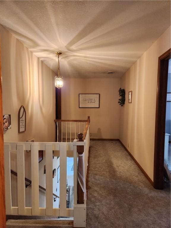 hallway with carpet, baseboards, a textured ceiling, an upstairs landing, and a chandelier