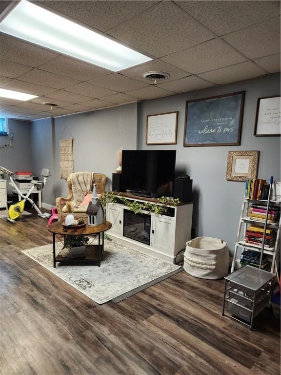 living room featuring visible vents, a paneled ceiling, baseboards, and wood finished floors