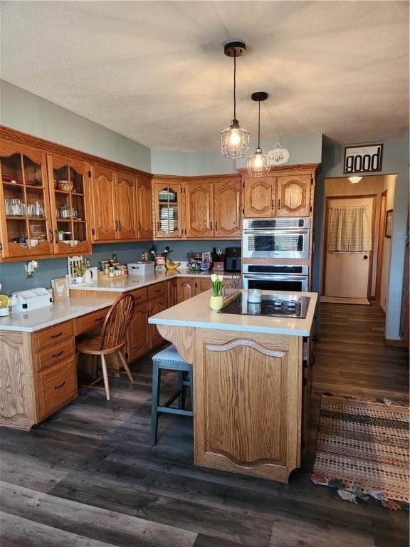 kitchen with glass insert cabinets, light countertops, brown cabinets, dark wood-style floors, and black electric cooktop