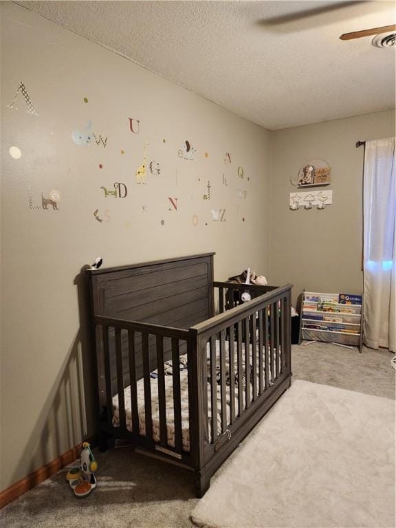 carpeted bedroom featuring a crib, a textured ceiling, and a ceiling fan