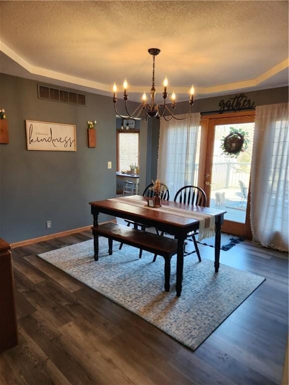 dining room featuring dark wood finished floors, visible vents, a textured ceiling, and a raised ceiling