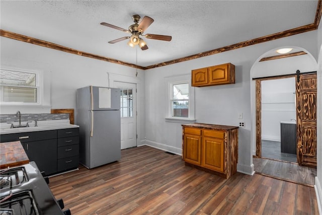 kitchen featuring dark wood finished floors, freestanding refrigerator, a barn door, ceiling fan, and a sink