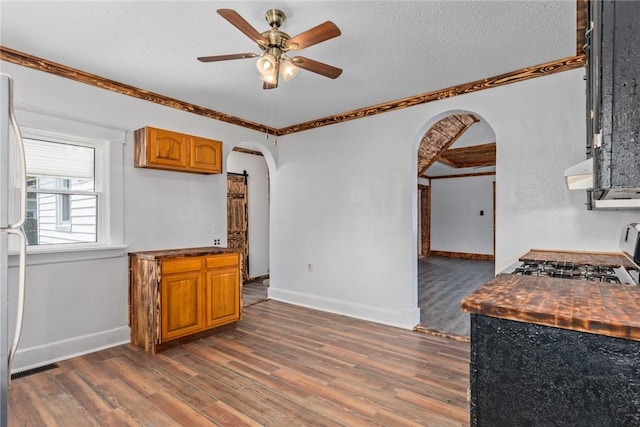 interior space with brown cabinetry, arched walkways, ceiling fan, and range with gas stovetop
