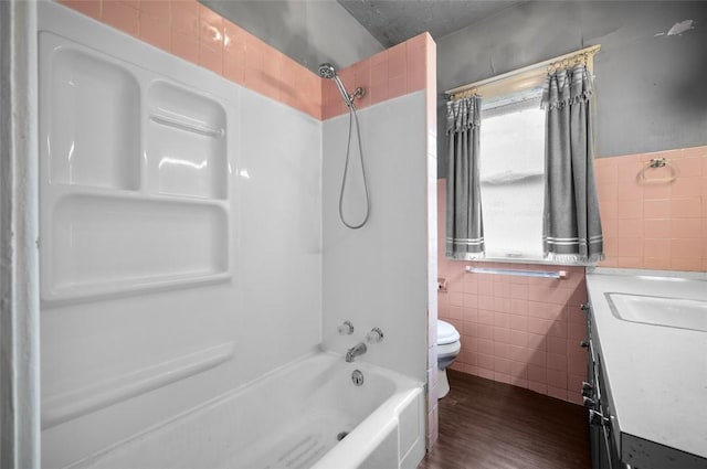 bathroom featuring tile walls, toilet, vanity, wood finished floors, and shower / bathing tub combination