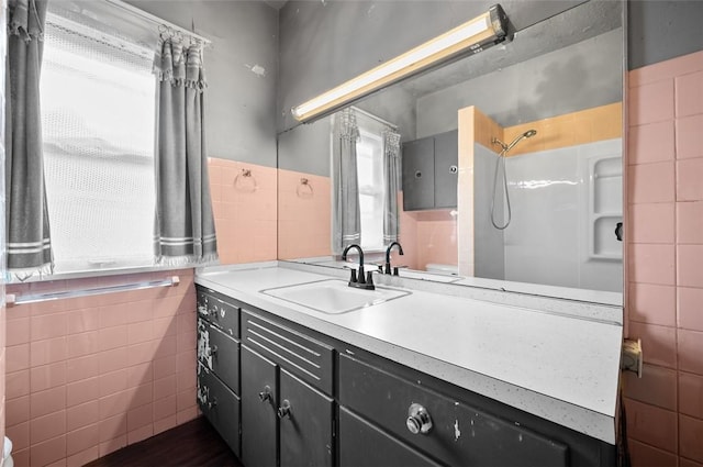 full bath with tile walls, walk in shower, vanity, and a wainscoted wall