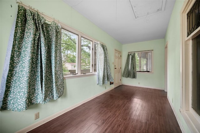 spare room with attic access, baseboards, a healthy amount of sunlight, and wood finished floors