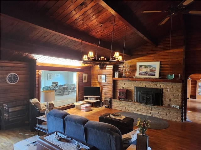 living area with beamed ceiling, wood walls, ceiling fan with notable chandelier, and wood finished floors