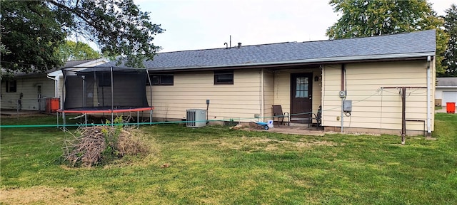 rear view of property featuring a yard, a trampoline, and central AC