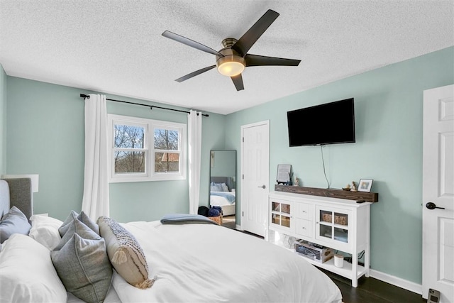 bedroom with dark wood-type flooring, a textured ceiling, baseboards, and a ceiling fan