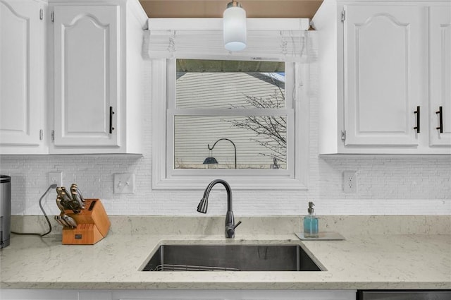 kitchen featuring light stone counters, pendant lighting, backsplash, white cabinetry, and a sink