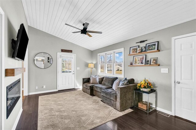 living room with a glass covered fireplace, dark wood-style flooring, visible vents, and vaulted ceiling