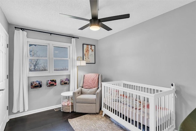 bedroom with a textured ceiling, ceiling fan, wood finished floors, baseboards, and a crib