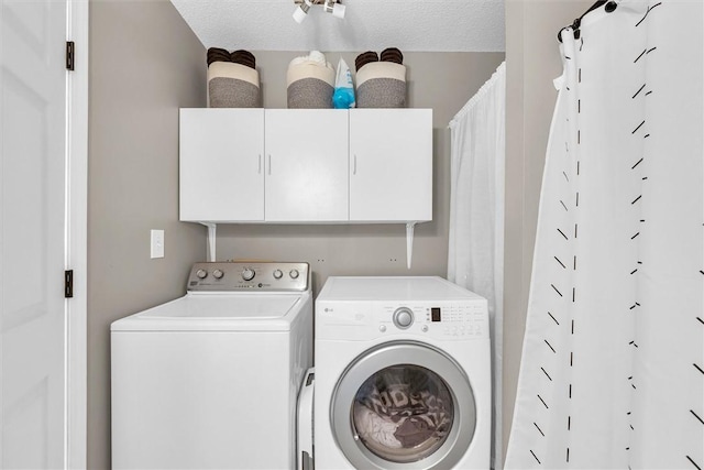 washroom with a textured ceiling, washing machine and dryer, and cabinet space