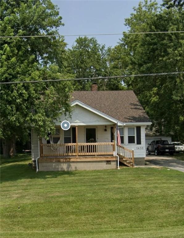 view of front facade with a chimney, a porch, a front lawn, and roof with shingles