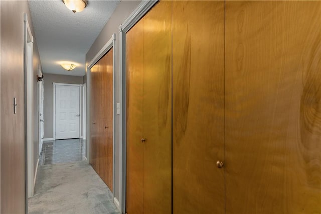 corridor with a textured ceiling, light carpet, and baseboards