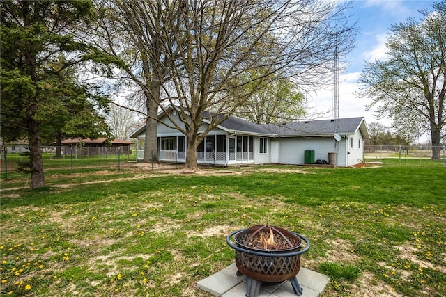 back of property with a sunroom, a fenced backyard, a fire pit, and a lawn