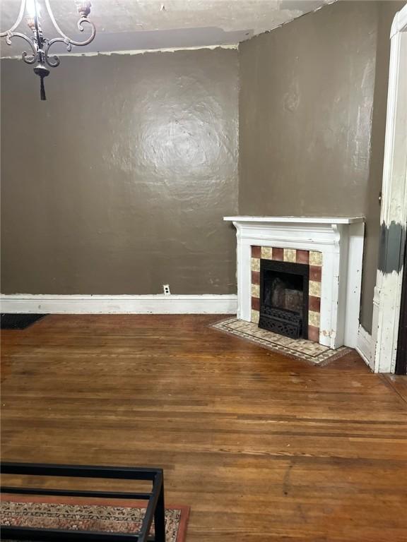 202 S College St, Blue Mound, IL 62513 - unfurnished living room featuring a tiled fireplace, baseboards, wood finished floors, and a chandelier