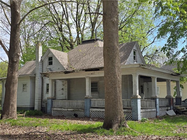 view of front of house featuring a chimney, a porch, and a shingled roof