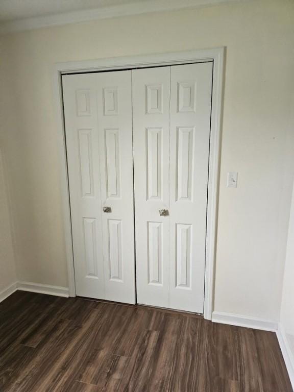 unfurnished bedroom featuring dark wood finished floors, a closet, crown molding, and baseboards