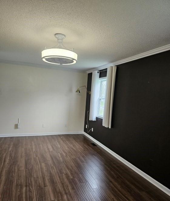empty room with ornamental molding, a textured ceiling, and dark wood-type flooring