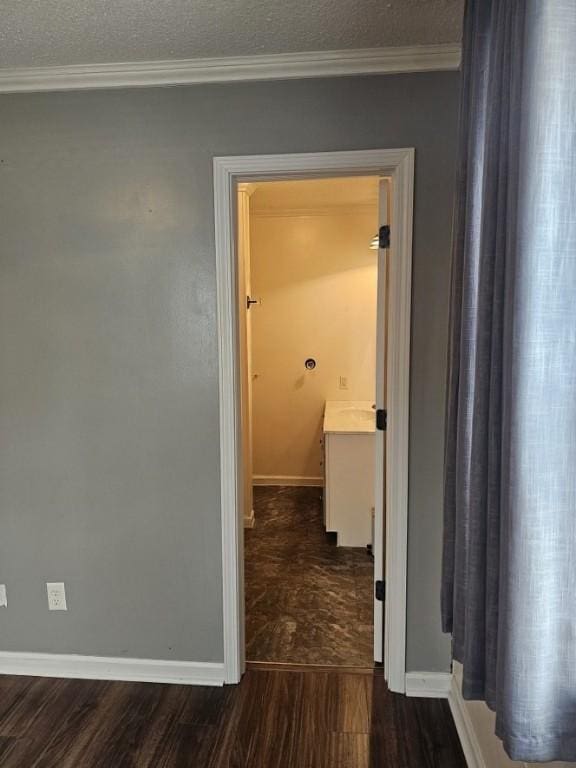 hallway with baseboards, wood finished floors, a textured ceiling, and crown molding