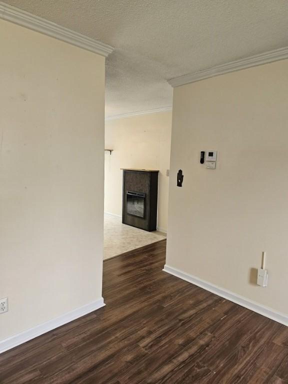 unfurnished room with a fireplace with flush hearth, baseboards, crown molding, and dark wood-style floors