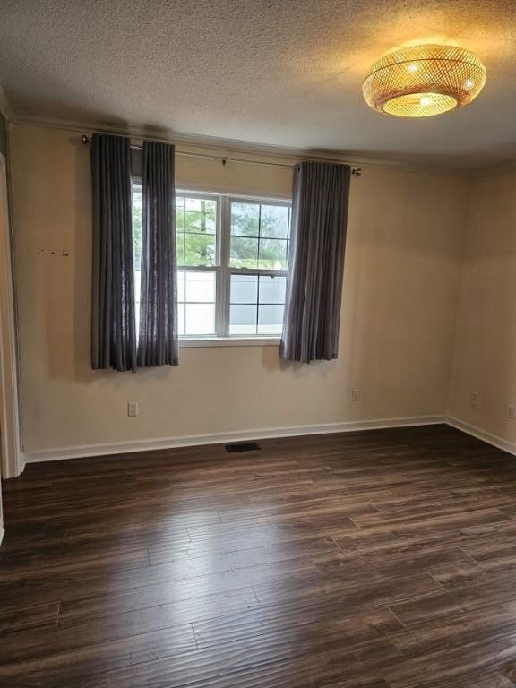 empty room featuring a textured ceiling, dark wood finished floors, baseboards, visible vents, and crown molding