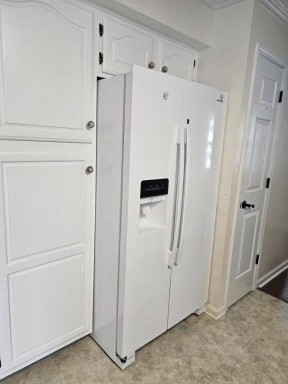 interior space featuring white refrigerator with ice dispenser, baseboards, and white cabinetry