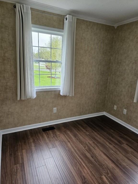 spare room featuring baseboards, visible vents, crown molding, and dark wood-style floors