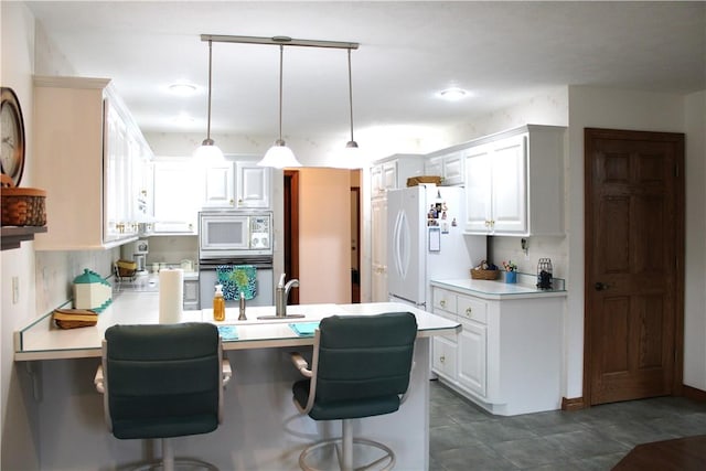 kitchen with light countertops, a breakfast bar area, a peninsula, white appliances, and decorative light fixtures