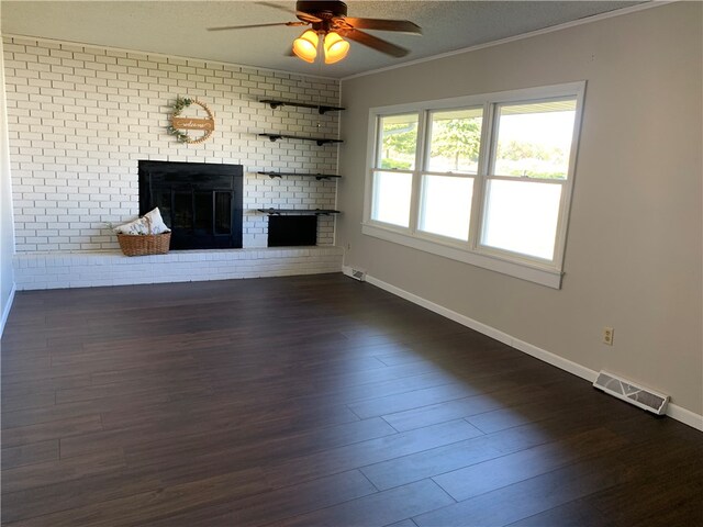 unfurnished living room featuring crown molding, ceiling fan, a fireplace, dark hardwood / wood-style flooring, and brick wall