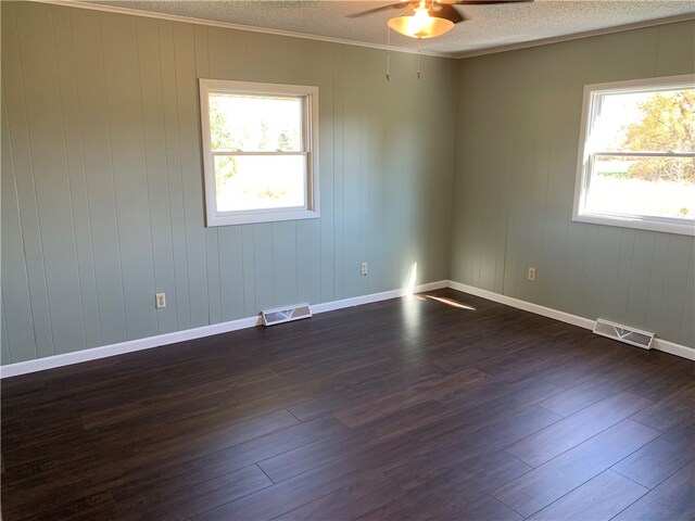 spare room with a wealth of natural light, wood walls, crown molding, and dark hardwood / wood-style floors