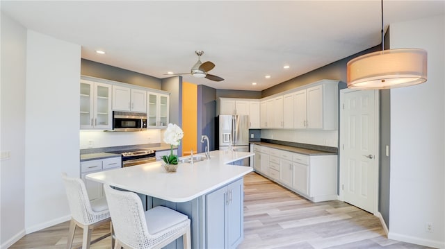 kitchen featuring white cabinets, stainless steel appliances, light wood-type flooring, a kitchen bar, and a sink